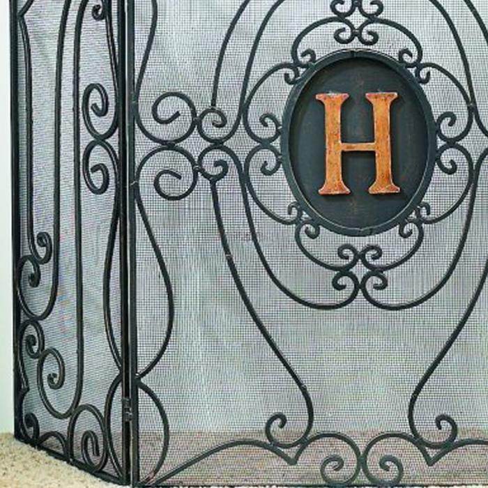 Close-up view of personalized monogram fireplace screen, highlighting the copper-toned letter H inset in an oval frame with elegant iron detailing.