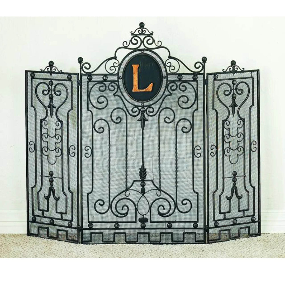 Three-panel wrought iron fireplace screen with ornate scrollwork and mesh backing, featuring a custom oval crest with the letter L in gold finish.
