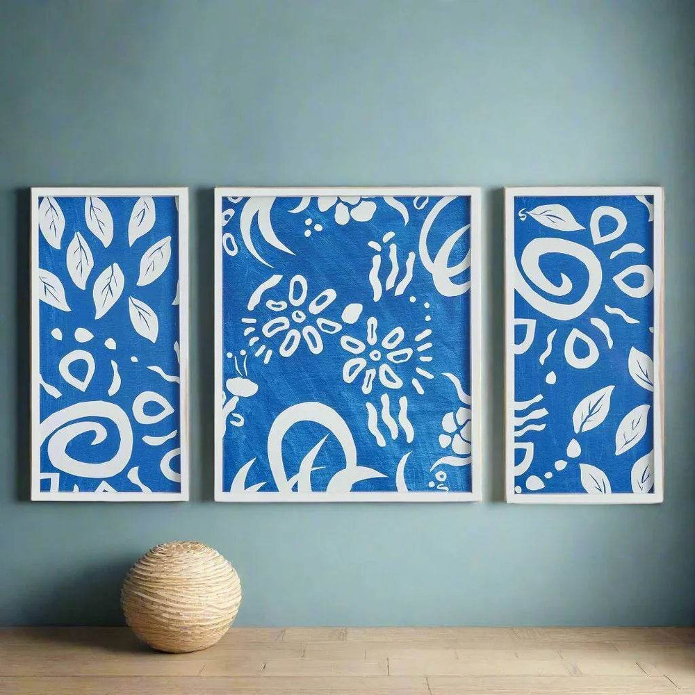 Blue and white abstract triptych with botanical motifs styled on a teal accent wall in coastal-inspired space.