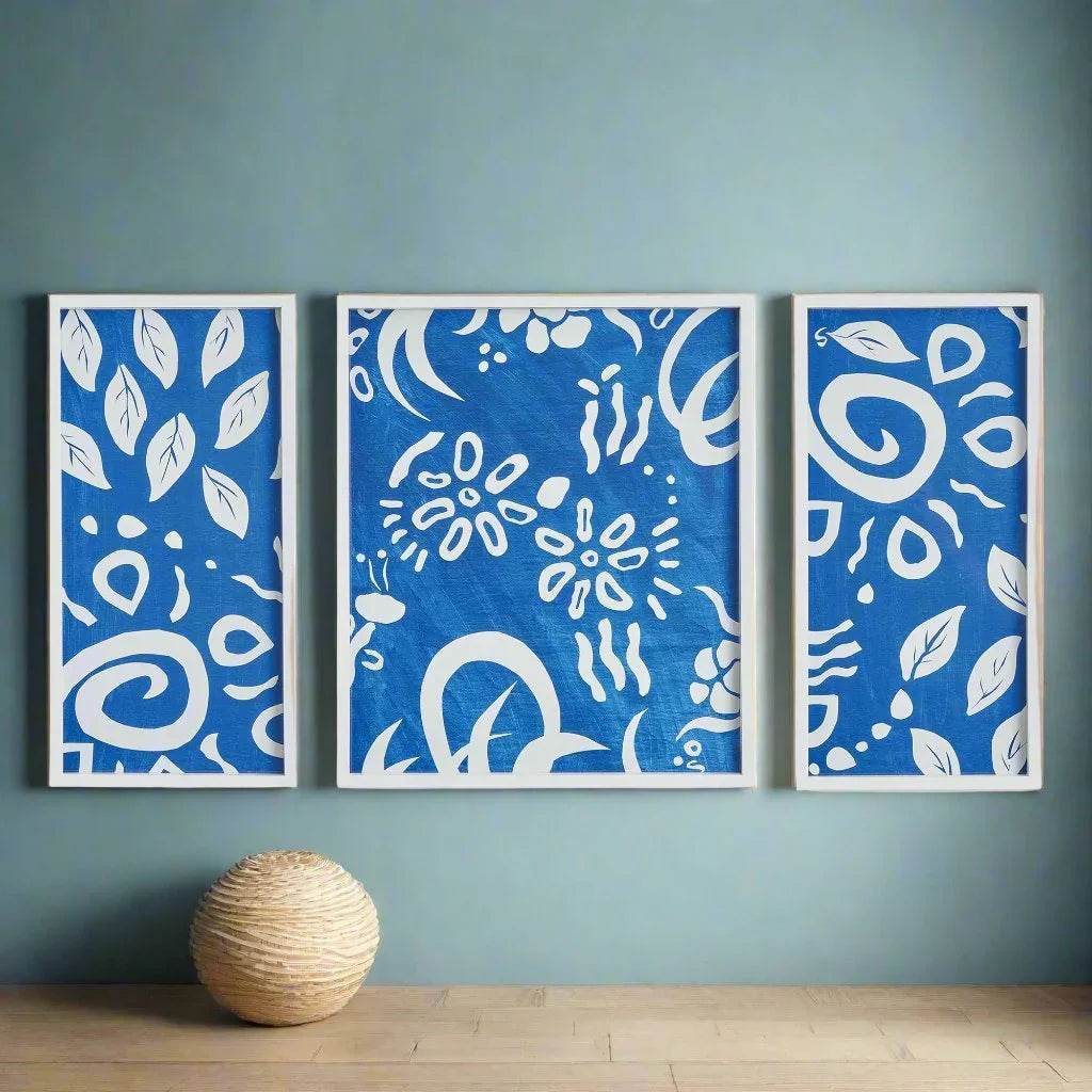 Blue and white abstract triptych with botanical motifs styled on a teal accent wall in coastal-inspired space.