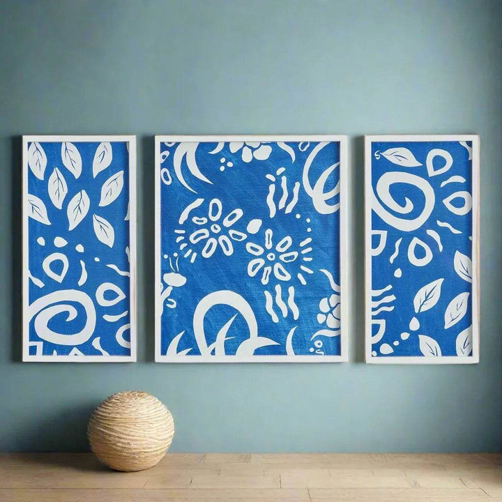 Blue and white abstract triptych with botanical motifs styled on a teal accent wall in coastal-inspired space.