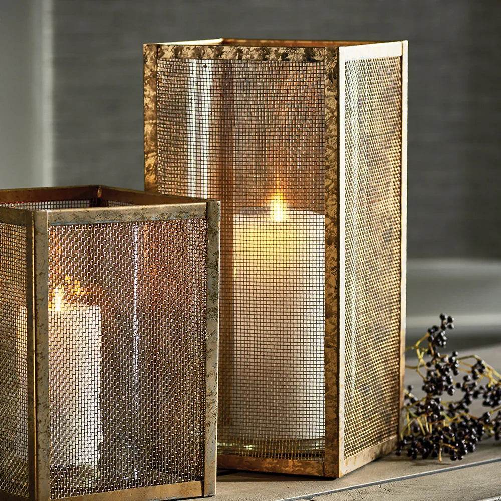 Tall gold mesh hurricane candle holder with candle lit, showing warm glow and shadows, perfect for entryway or living room styling.