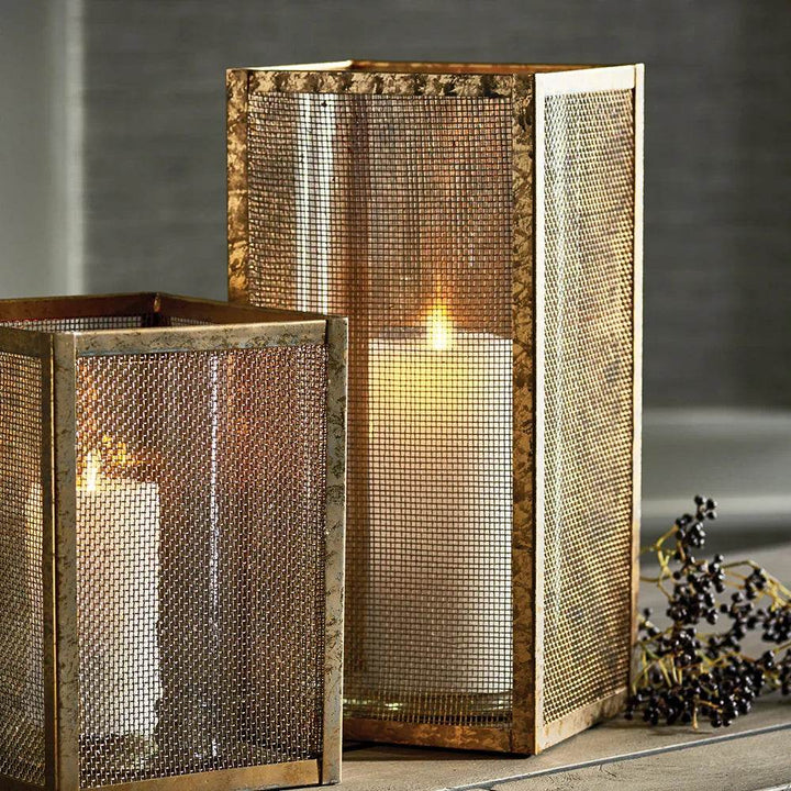 Tall gold mesh hurricane candle holder with candle lit, showing warm glow and shadows, perfect for entryway or living room styling.
