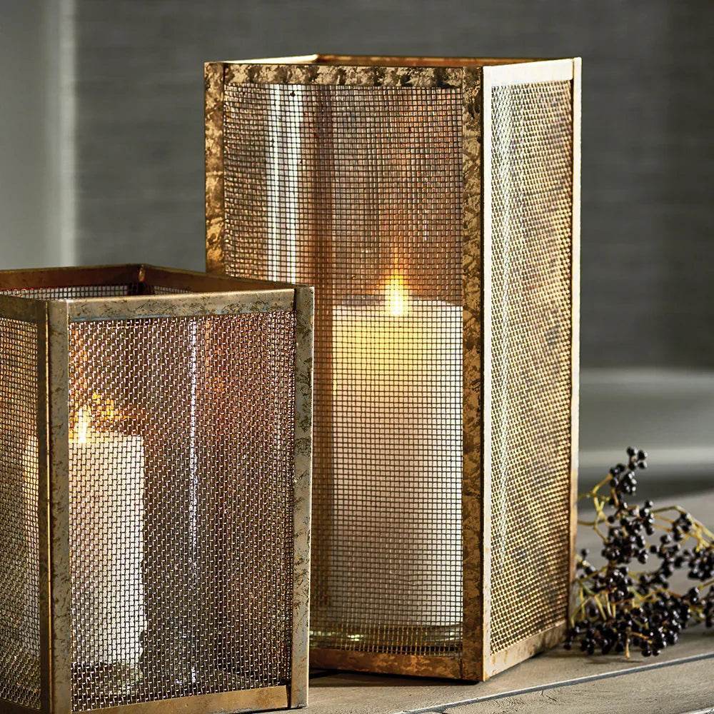 Tall gold mesh hurricane candle holder with candle lit, showing warm glow and shadows, perfect for entryway or living room styling.
