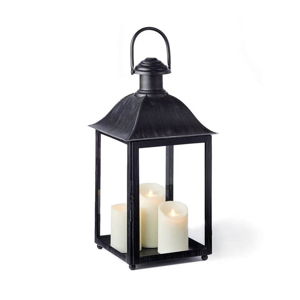 Studio view of black outdoor candle lantern with glass panels and lit candles inside