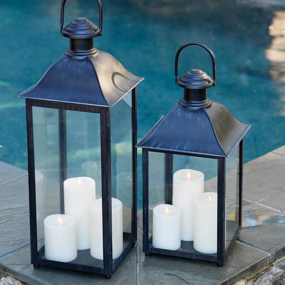 Set of black candle lanterns by the pool with candles glowing inside at dusk