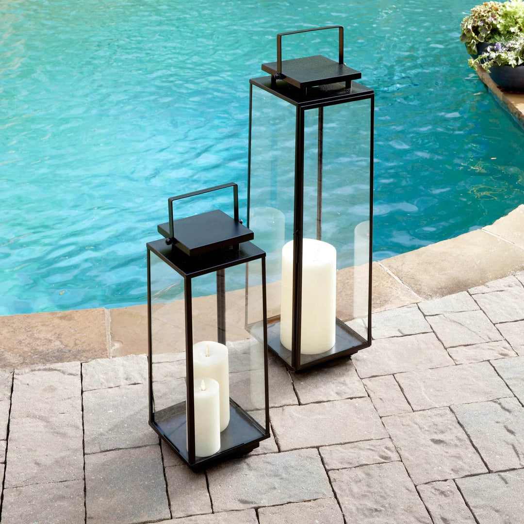 Pair of black stainless steel outdoor lanterns with glass panels, styled beside poolside seating and stone patio – Transitional