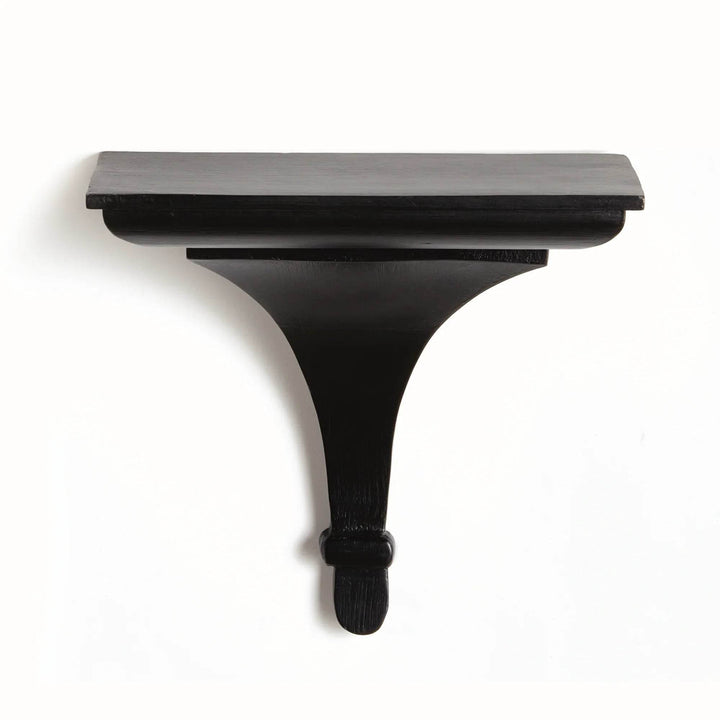 Matte black wood decorative bracket shelf on light textured plaster wall, styled with soft shadows and architectural contrast.