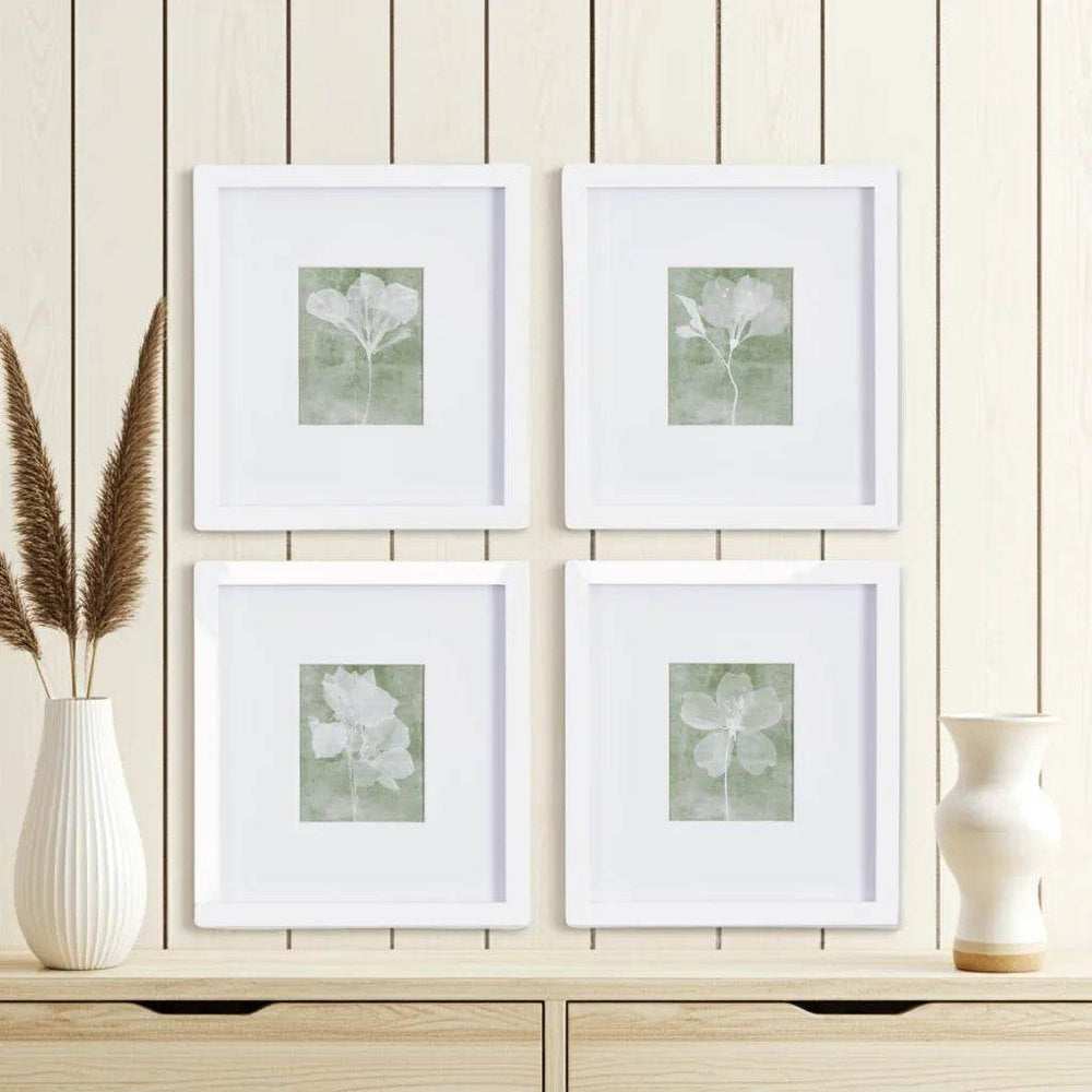 Close-up of framed green floral prints with white mats styled against neutral wood paneling