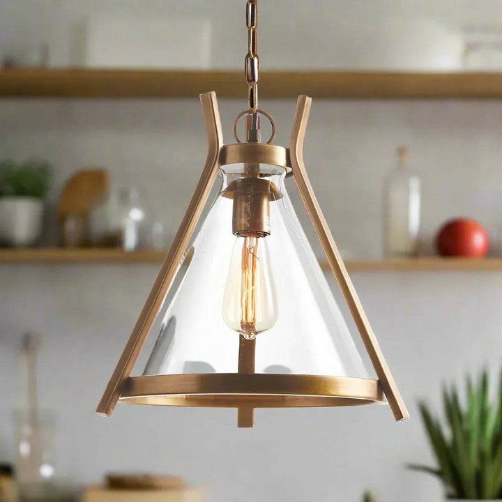 Lifestyle scene of brass pendant light with clear glass shade illuminating contemporary kitchen counter—modern industrial décor accent