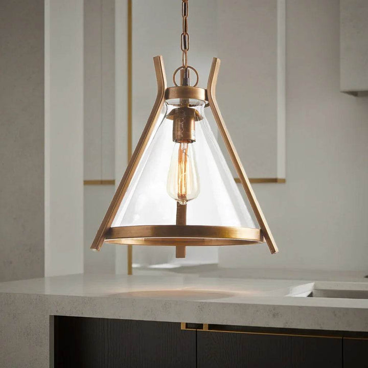 Studio shot of brass pendant light suspended from chain, displaying Edison bulb through clear glass shade for warm industrial glow