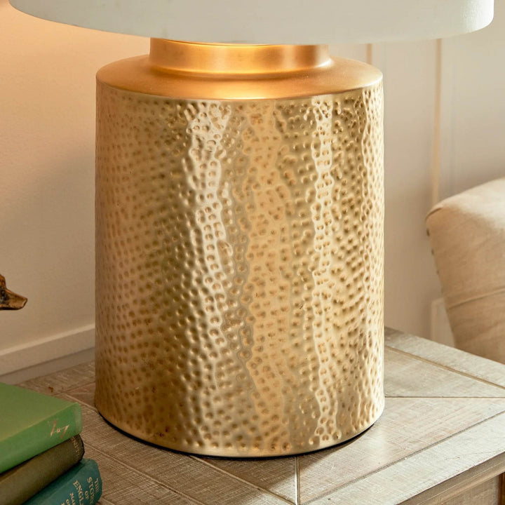 Hammered brass table lamp with light on, casting warm coastal-inspired glow