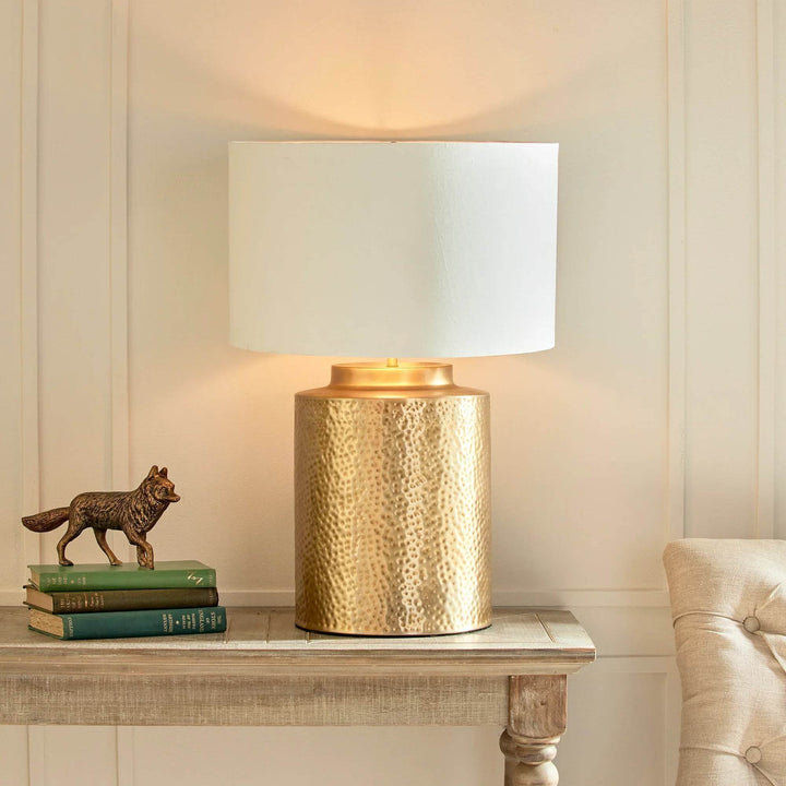 Hammered brass lamp on side table styled with neutral decor in organic luxe interior