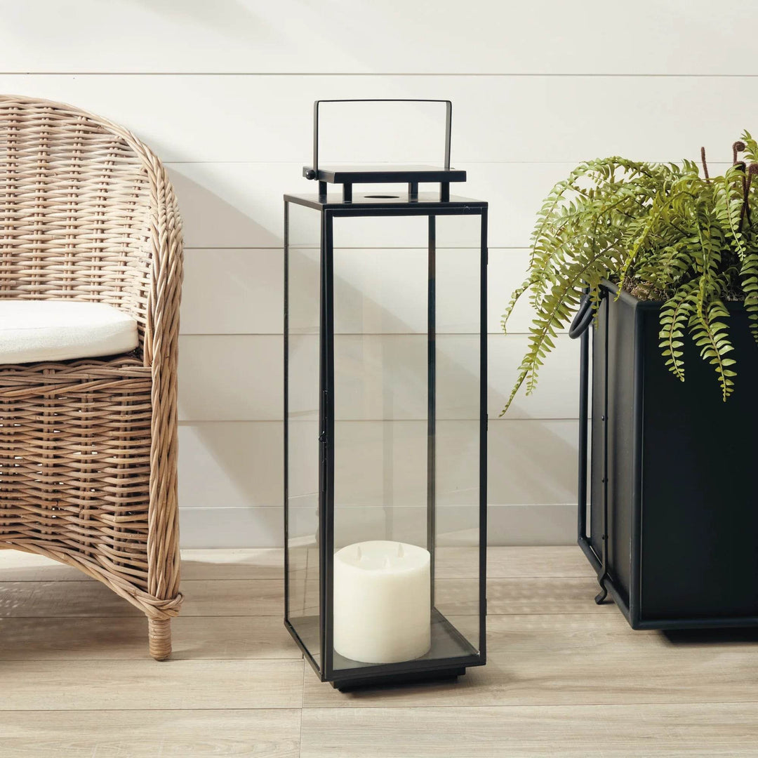 Large rectangular black outdoor lantern with glass sides, shown near wicker chair and greenery for porch or entryway – Transitional