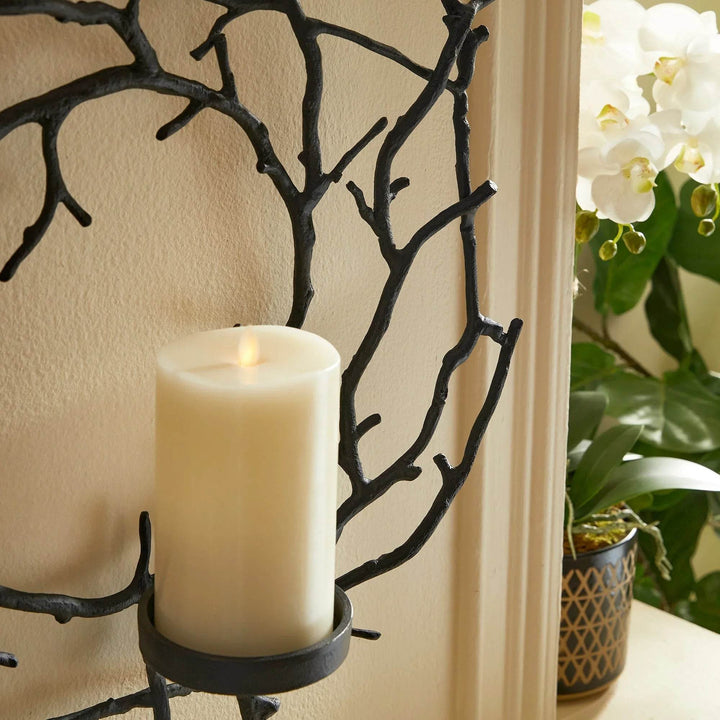 Close-up of LED pillar candle seated in matte black wall candle holder with organic twig frame.