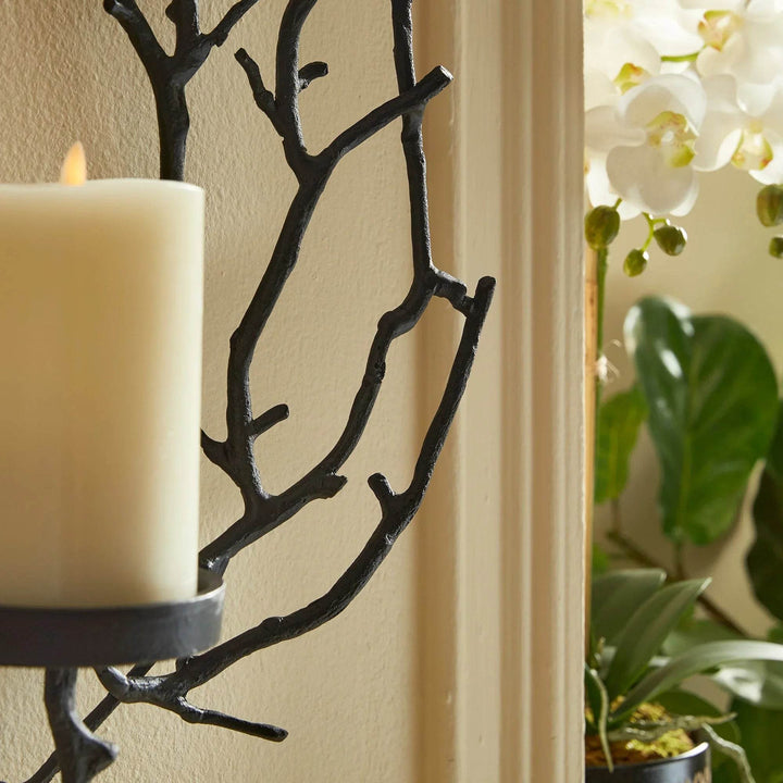 Detailed branch motif of rustic matte black candle holder styled next to blooming white orchids.