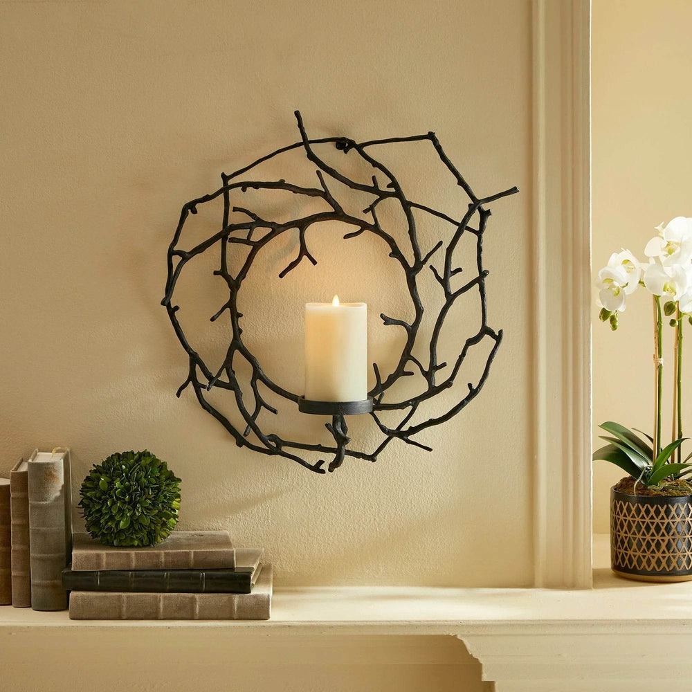Sculptural black aluminum candle holder styled above a mantel in a rustic minimalist interior.