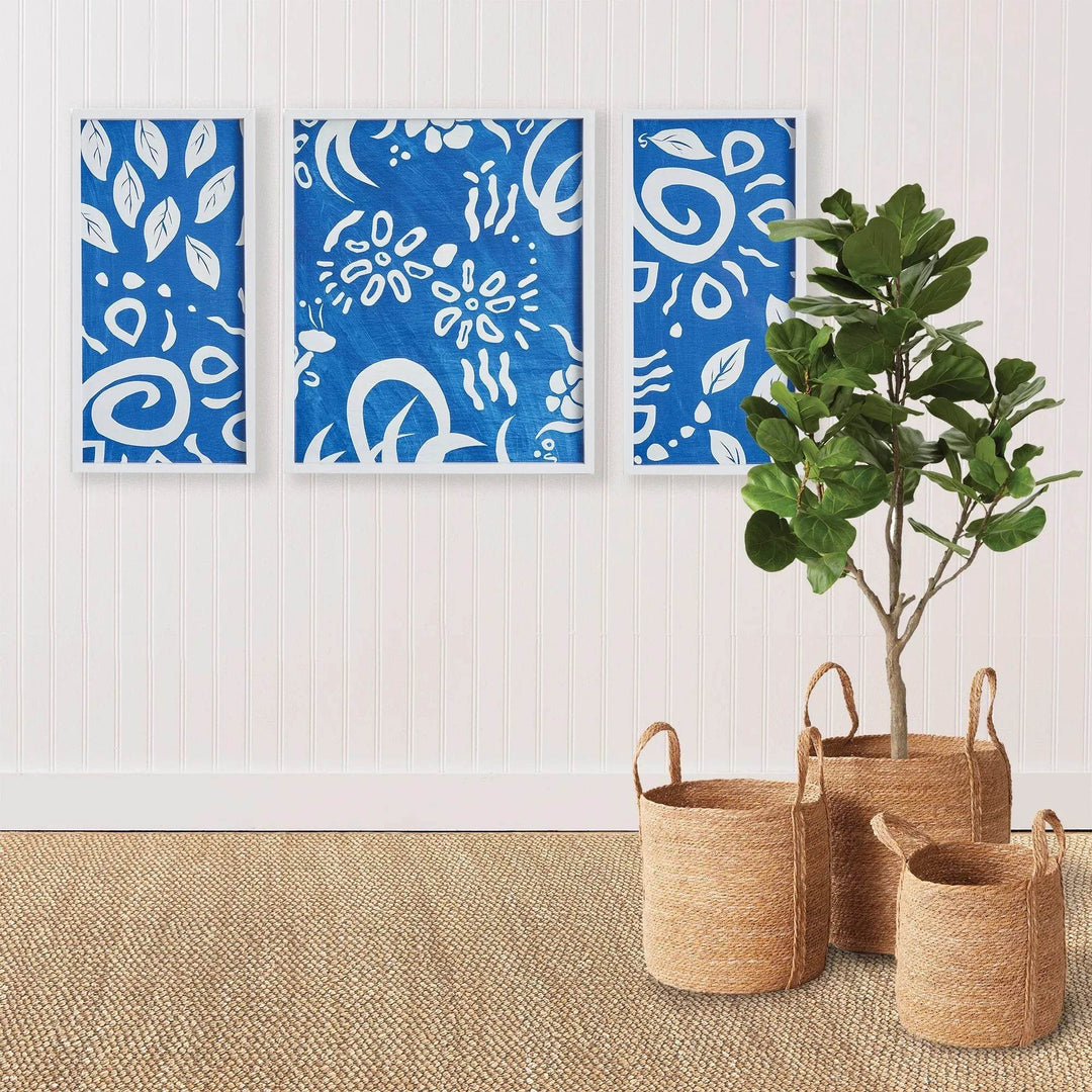 Blue abstract triptych wall art framed above jute rug and seagrass baskets, styled in a modern coastal room