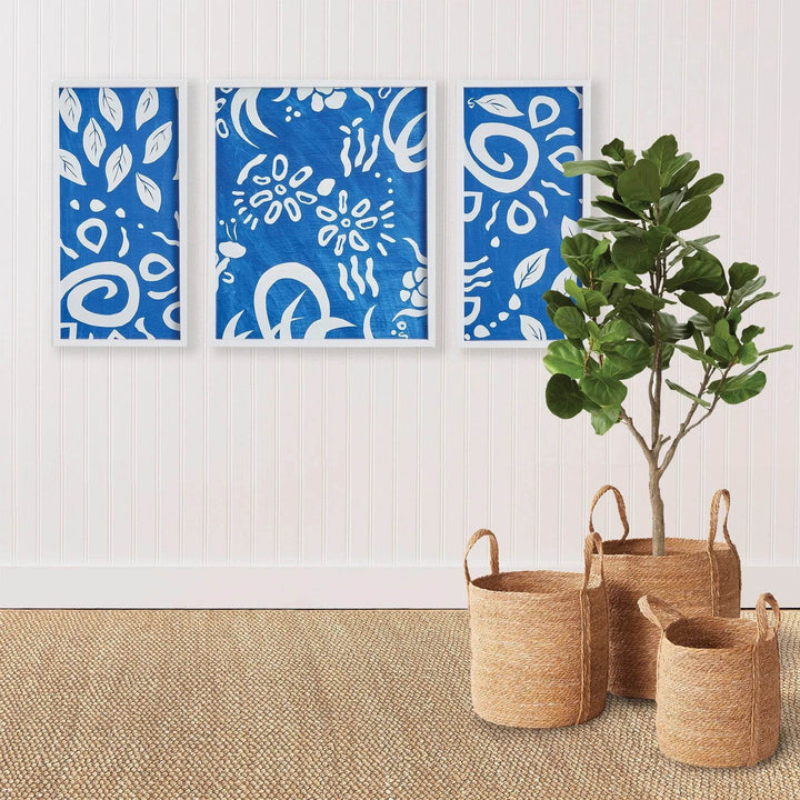 Blue abstract triptych wall art framed above jute rug and seagrass baskets, styled in a modern coastal room
