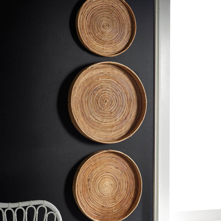 Close-up of circular woven cane tray hung on dark wall - boho natural basket wall accent
