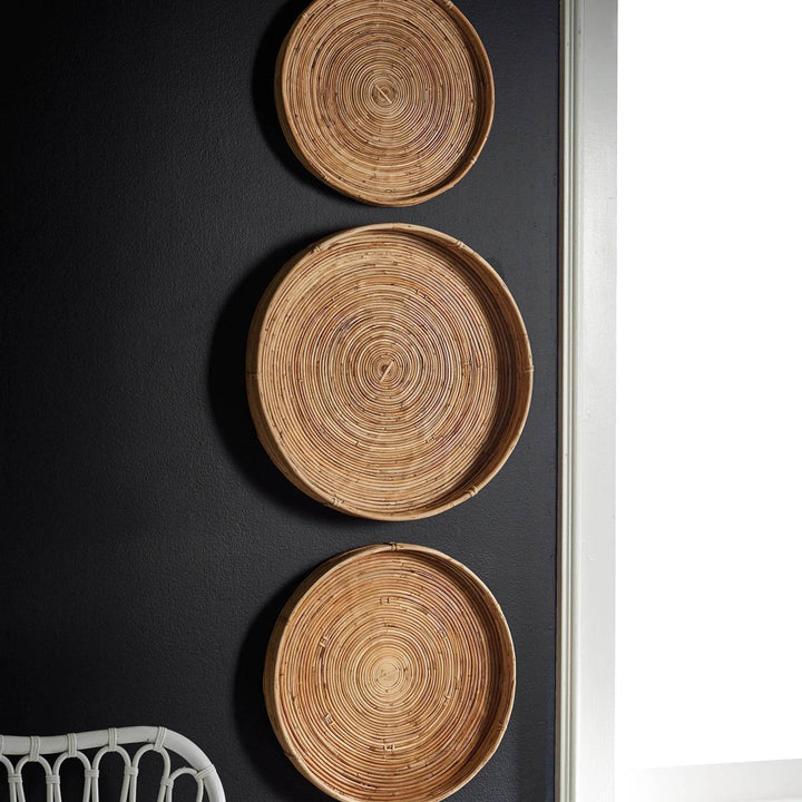 Close-up of circular woven cane tray hung on dark wall - boho natural basket wall accent