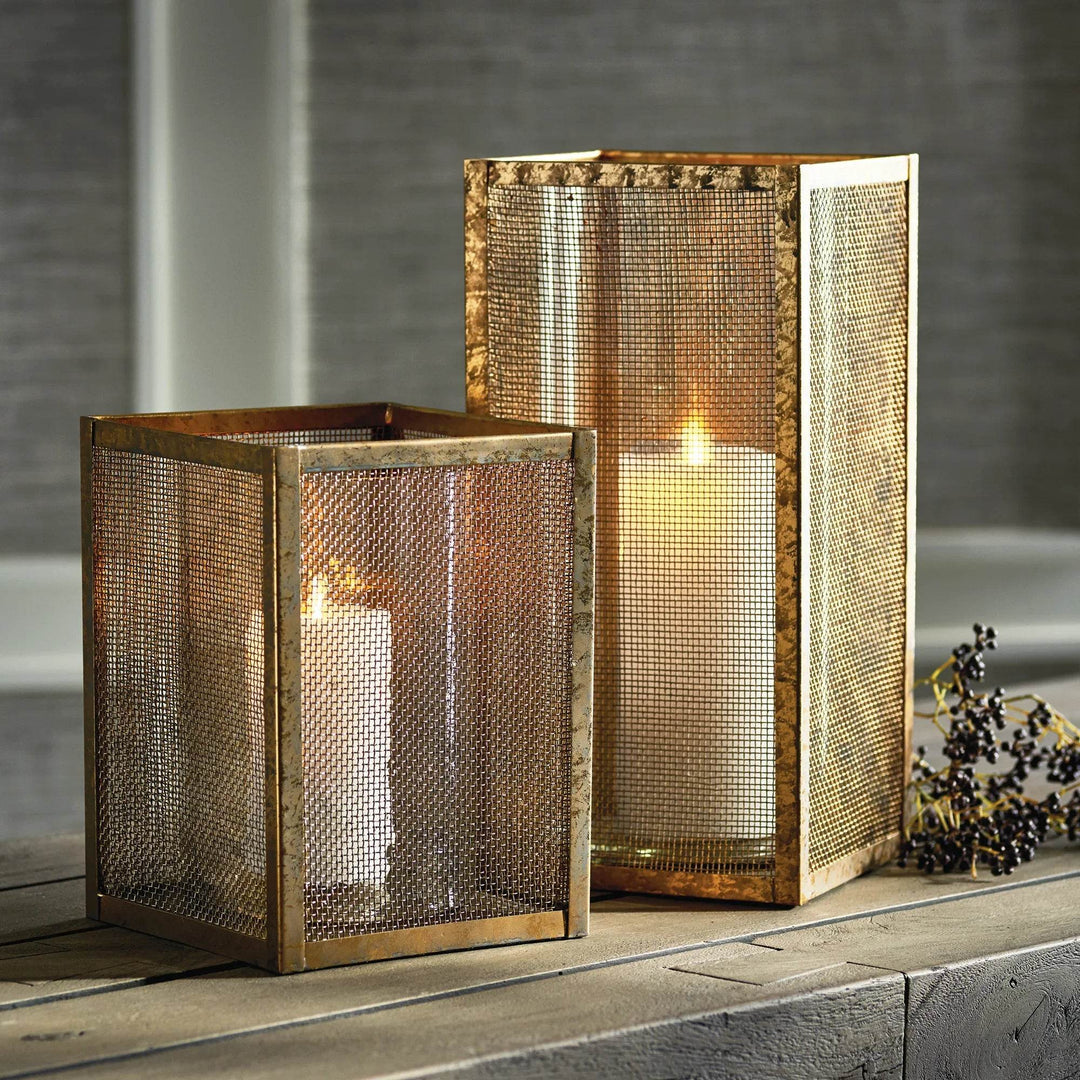 Pair of gold mesh hurricane candle holders, 10 inch and 15 inch, styled on table with lit candles for modern industrial decor.