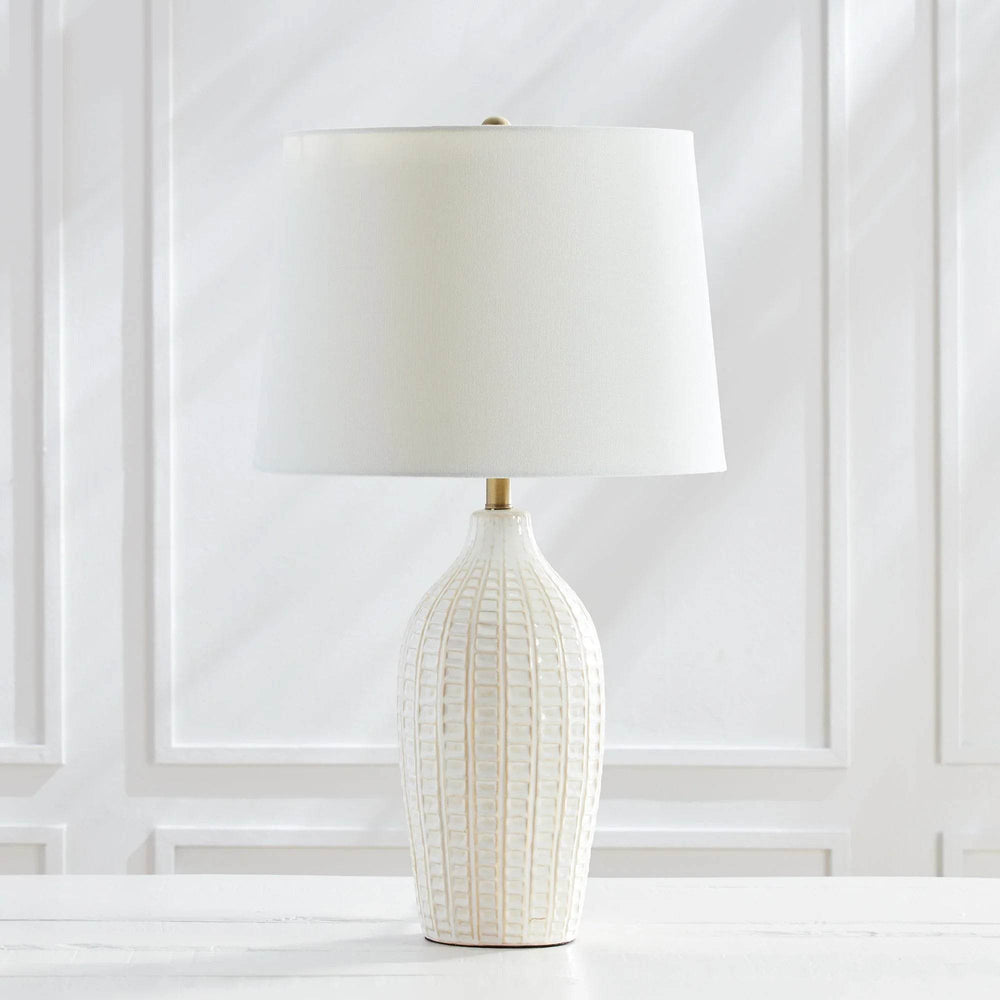 Studio side view of tall white ceramic table lamp with pressed pattern and brass accents