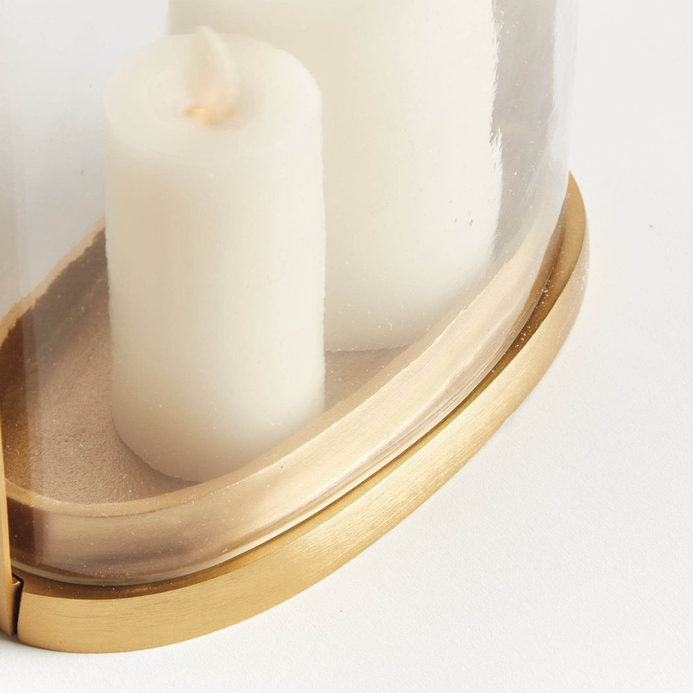 Close-up of the small transitional brass and glass hurricane candle holder showing matte brass oval base and candle detail.