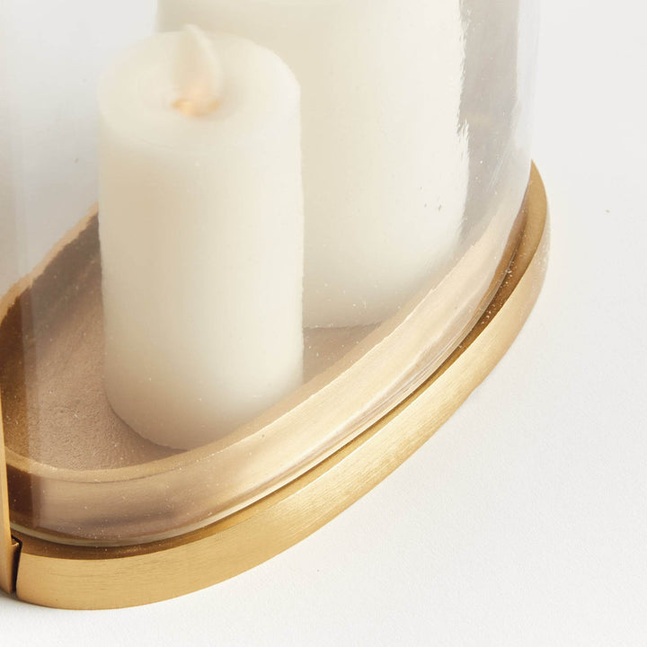 Close-up of the small transitional brass and glass hurricane candle holder showing matte brass oval base and candle detail.