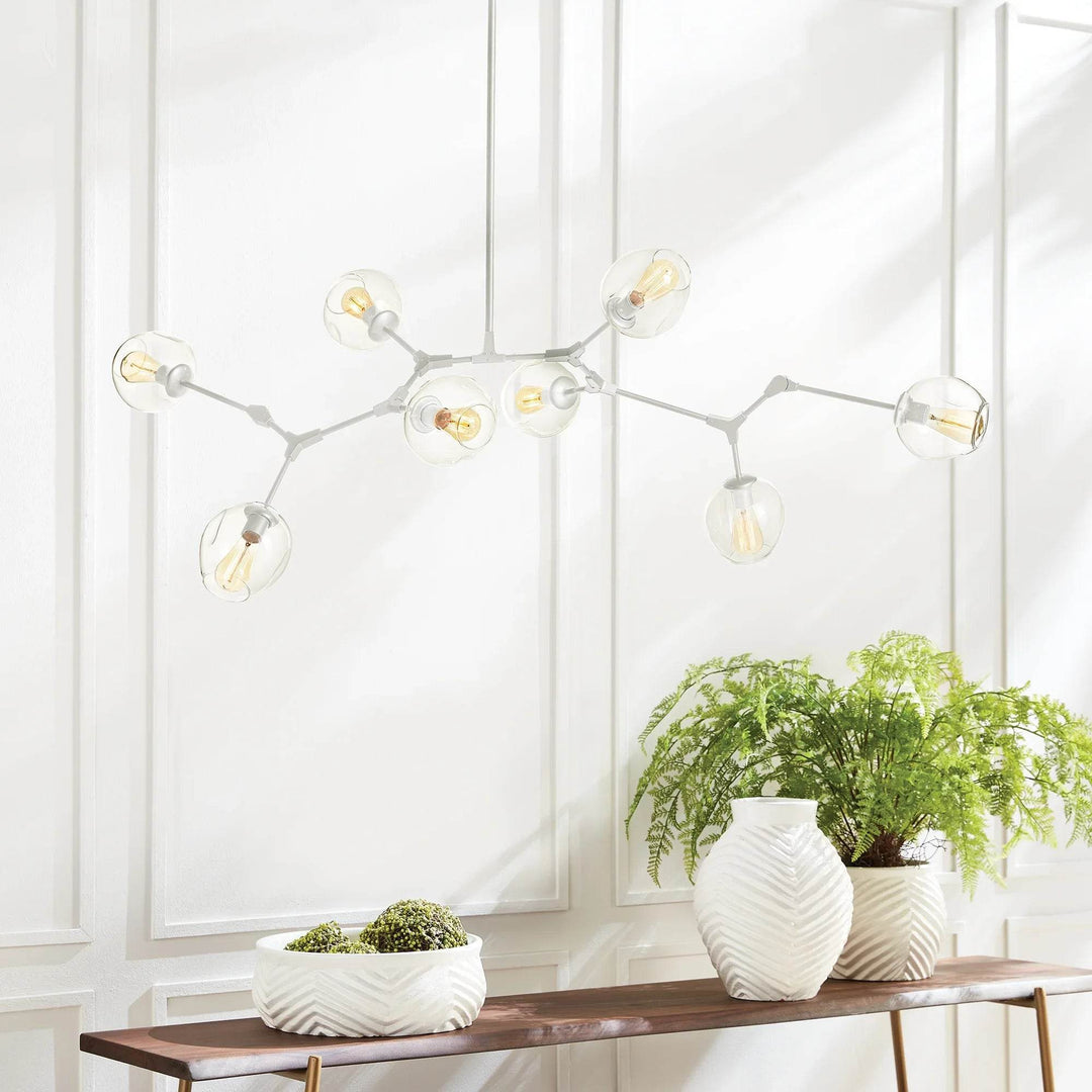 White mid-century modern chandelier styled above a wood console with greenery in a bright dining space.