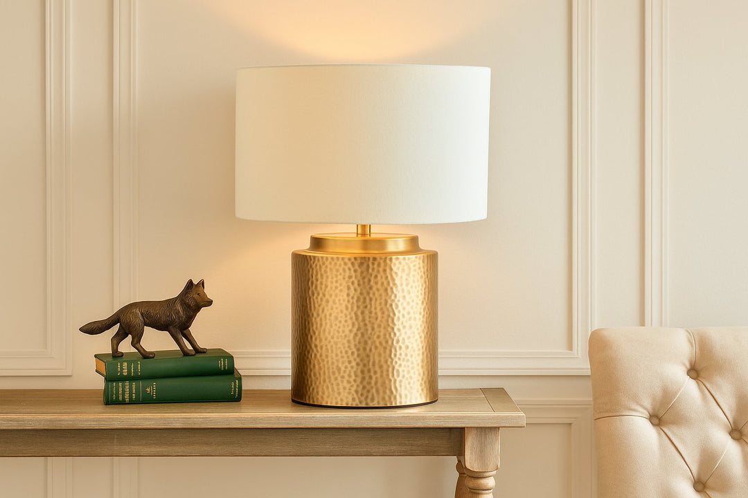 Coastal transitional interior with a hammered brass table lamp, neutral panelled wall, and natural wood console table styled with vintage books.