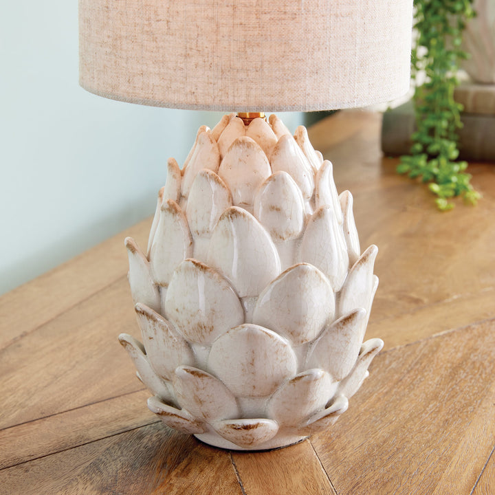 As an expert in this industry, I have designed a ceramic table lamp inspired by the natural beauty of an artichoke. Carefully hand-finished with antiqued edges, this masterpiece adds an elegant touch to traditional spaces. Paired with a natural linen shade, it is the perfect choice to elevate any room.