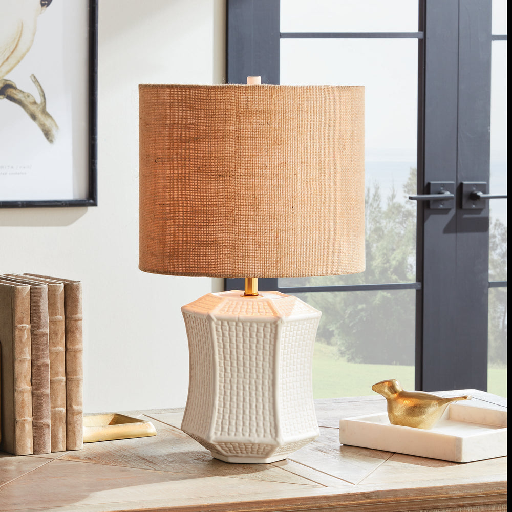 The ceramic base of this table lamp has a unique texture that resembles woven fabric, making it a defining feature of the piece. Its paneled design and impressive size make it a stand-out focal point for any transitional setting. Available in white and tan, this lamp adds an elegant touch to any room.