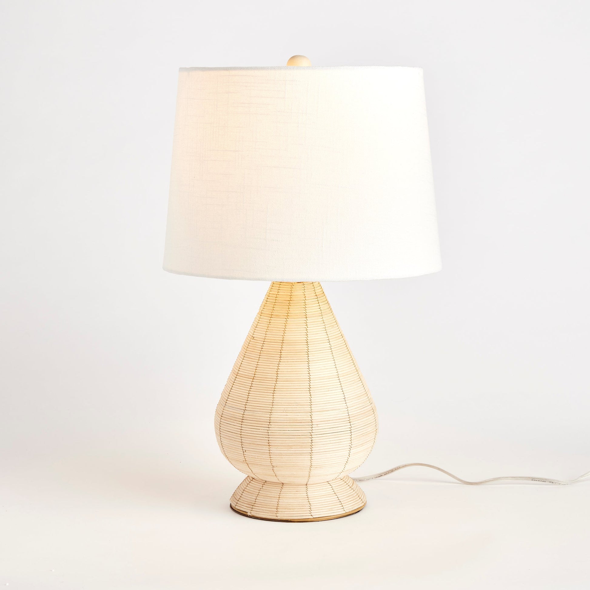 This table lamp features a whitewash cane rattan weave and each piece has its own unique color variations. It is a timeless piece complemented by a wide cylindrical shade, perfect for any bedroom, living room, or study. The lamp is handcrafted and features a European-style shade, making it a one-of-a-kind addition to any space.