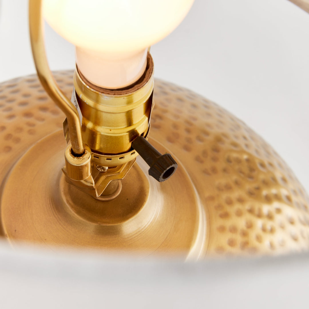 Enhance any room with the elegant style of Tara Gold &amp; White Table Lamp Small. The warm brass round base exudes a luxurious feel, while the crisp white linen drum shade offers a gentle radiance. Crafted from hammered iron and featuring unique handmade elements, this lamp is the perfect addition to any modern space.