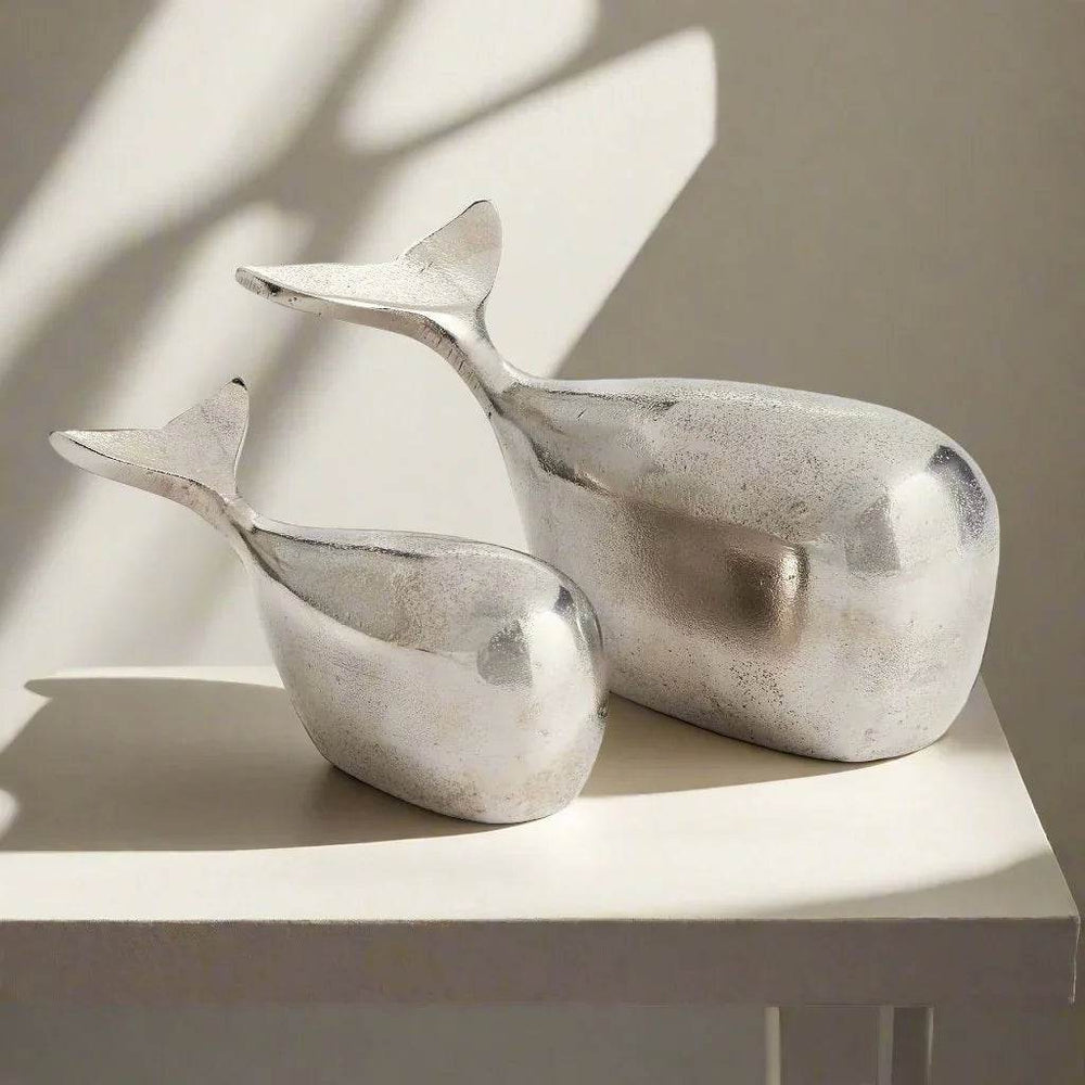 Two metallic whale sculptures on a light surface with a neutral background