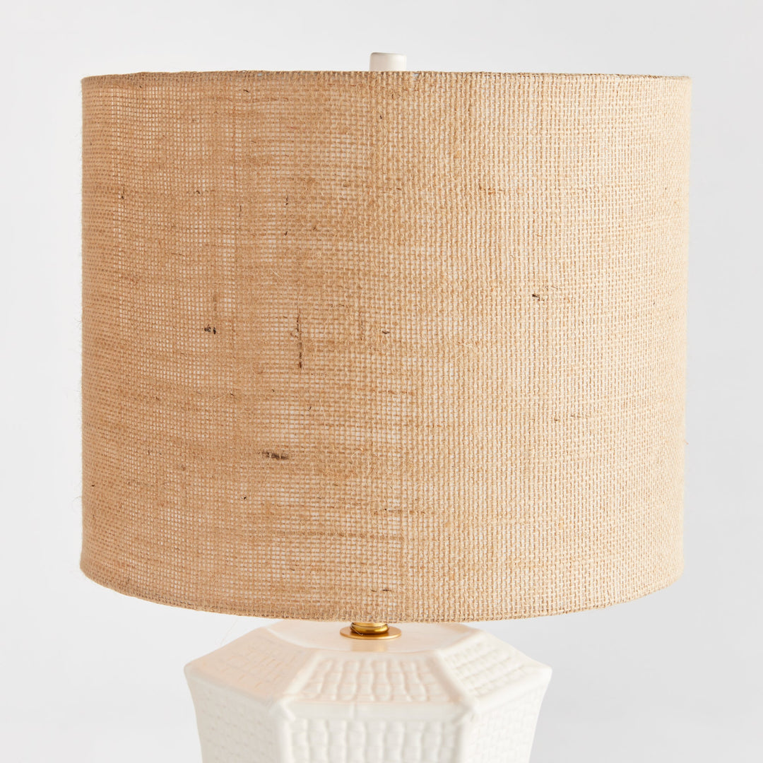 The ceramic base of this table lamp has a unique texture that resembles woven fabric, making it a defining feature of the piece. Its paneled design and impressive size make it a stand-out focal point for any transitional setting. Available in white and tan, this lamp adds an elegant touch to any room.