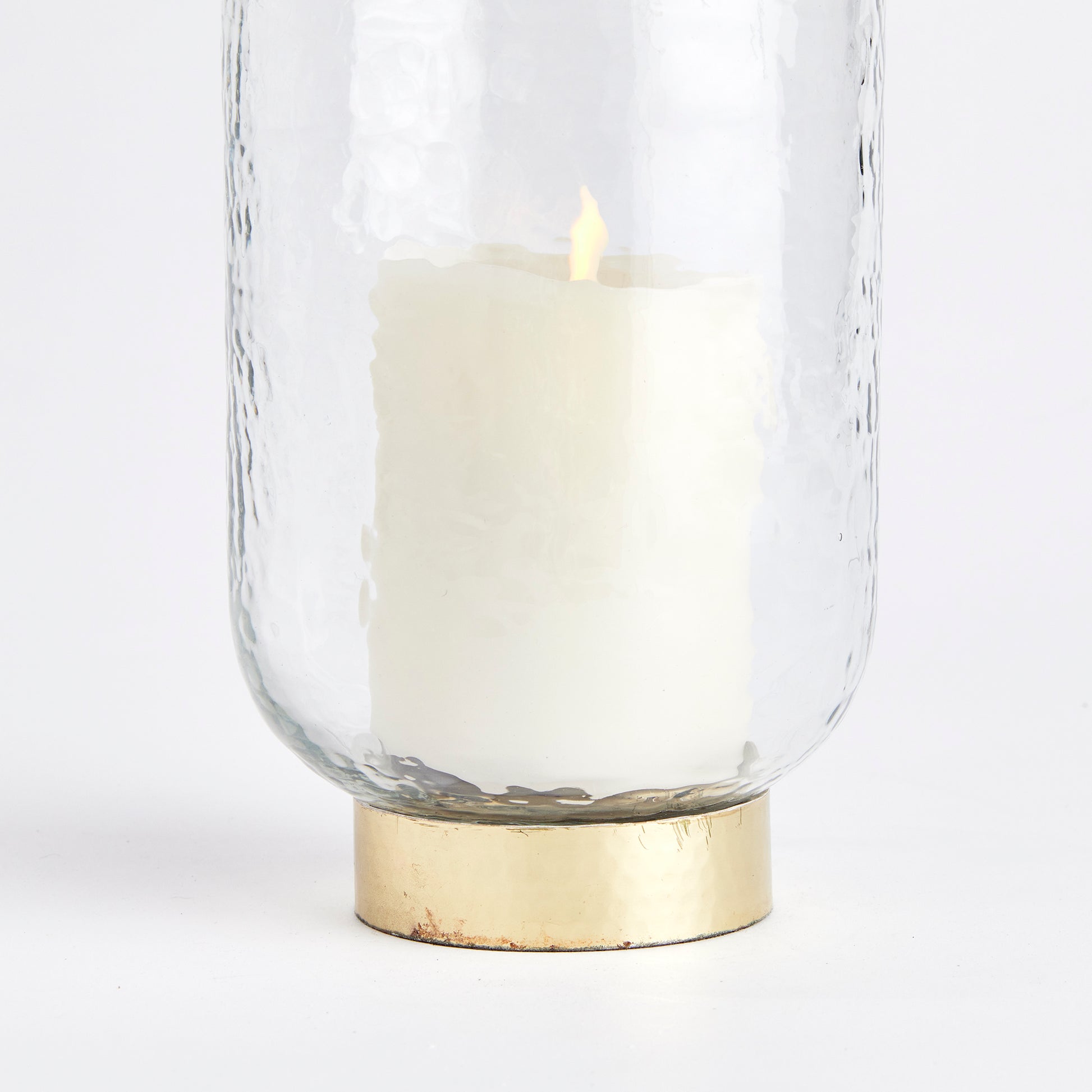 Featuring a thick, hammered glass and a unique melted uneven edge, the Amira Gold Hurricane Medium Candle Holder adds an artisanal touch to any space. Its finishing touch is the elegant hammered gold rim base, making it a sophisticated accent for console, bookshelf, or mantel. Crafted with expert skill, this hurricane is a true testament to fine craftsmanship.