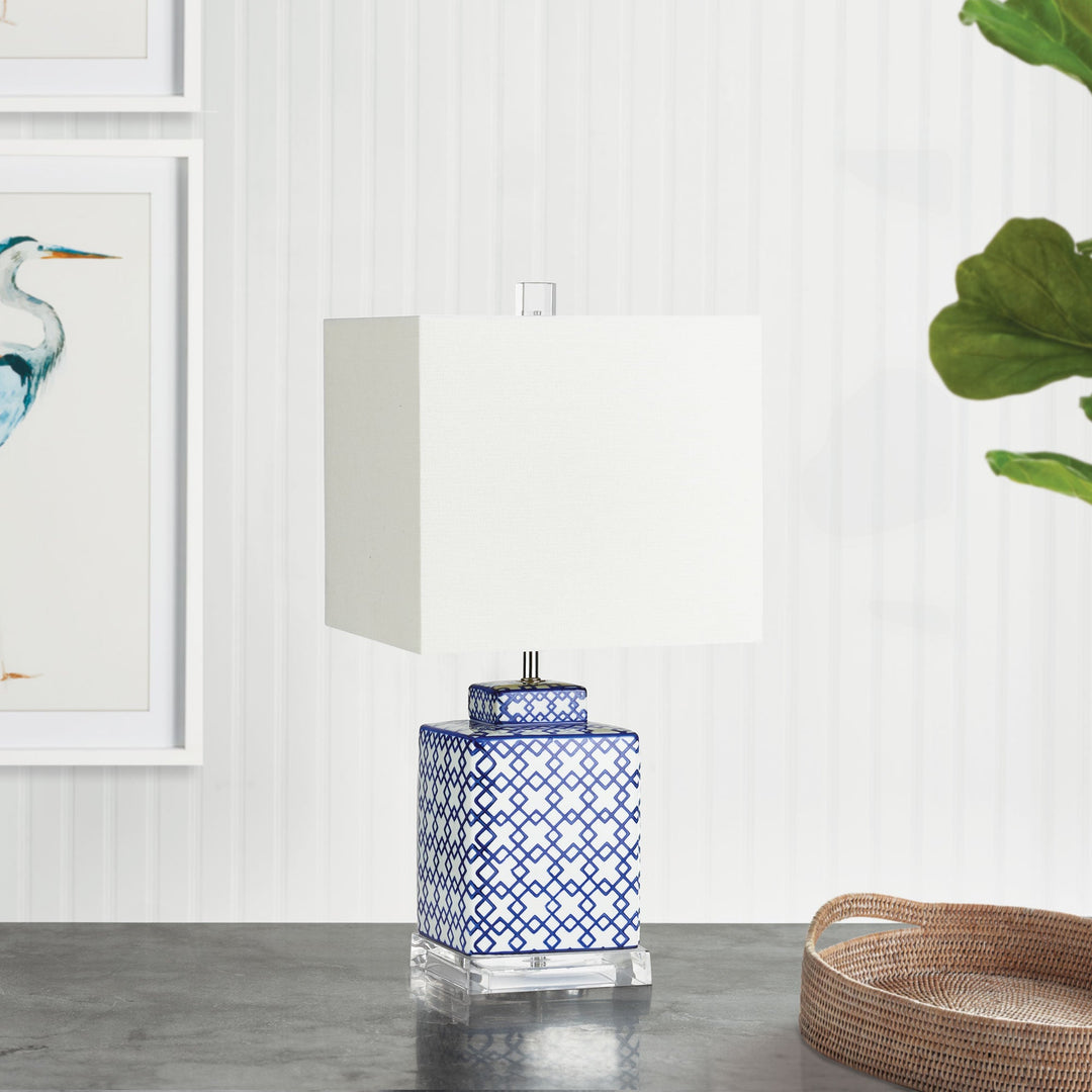 This table lamp boasts a striking square shape and bold pattern, making it a sophisticated addition to any living area. Whether placed on a side table, console, or shelf, it offers a stunning way to add light to the room. Crafted with an acrylic stand, ceramic base, and linen shade, it is the perfect choice for your living room.