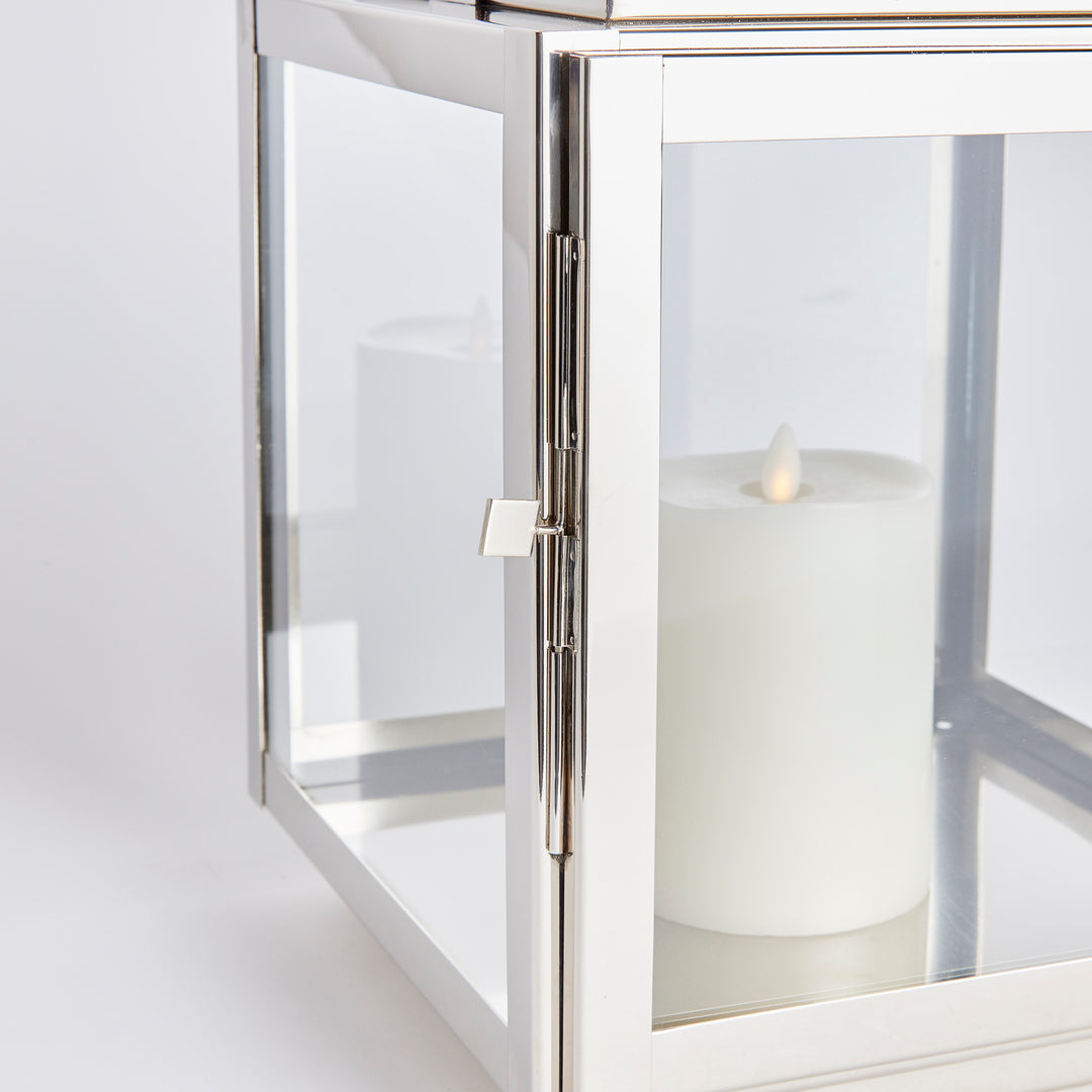 Elevate your outdoor space with the Adwin Outdoor Silver Garden Lantern Medium. The uniquely designed lantern features a teak handle, wide glass panes, and an exclusive chrome design. Its tailored square profile adds a modern touch to any patio, porch, or lanai, making it a must-have for any garden or outdoor area.