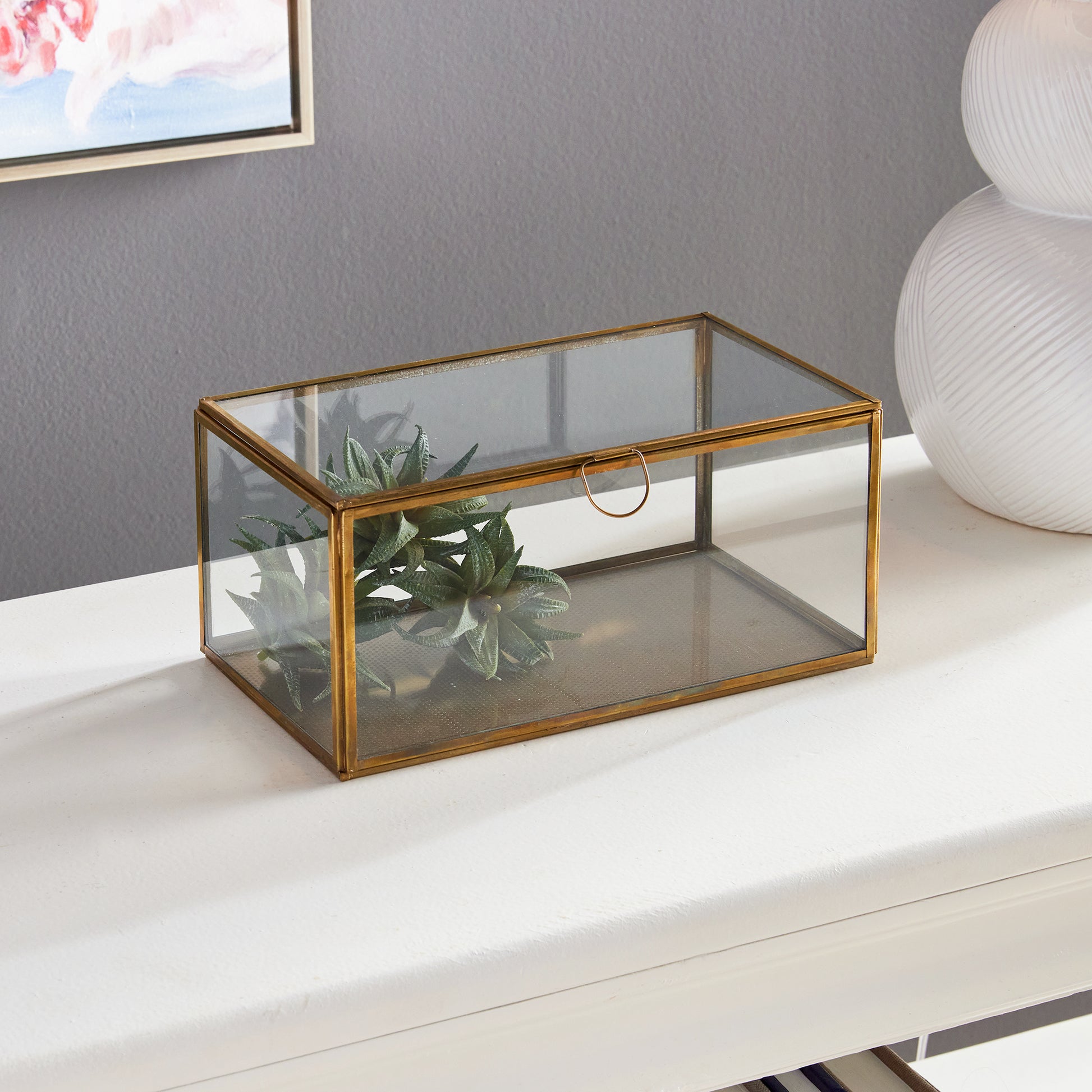 Expertly crafted with a combination of glass and brass, the Arwen Rectangular Antique Brass Display Box is designed to securely hold and protect your most cherished mementos. A sleek loop handle prevents fingerprints from marking the glass, keeping your keepsakes pristine.