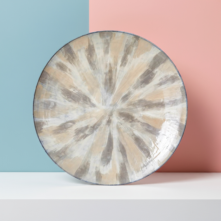 36 inch round enameled iron wall plate with painted cream and taupe rays, shown on color-block studio surface – Transitional