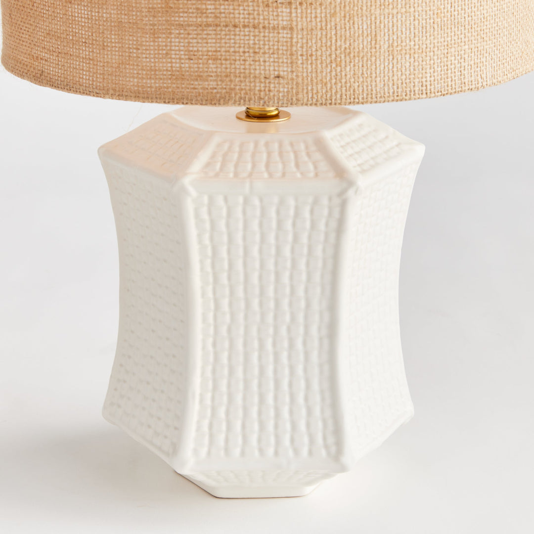 The ceramic base of this table lamp has a unique texture that resembles woven fabric, making it a defining feature of the piece. Its paneled design and impressive size make it a stand-out focal point for any transitional setting. Available in white and tan, this lamp adds an elegant touch to any room.