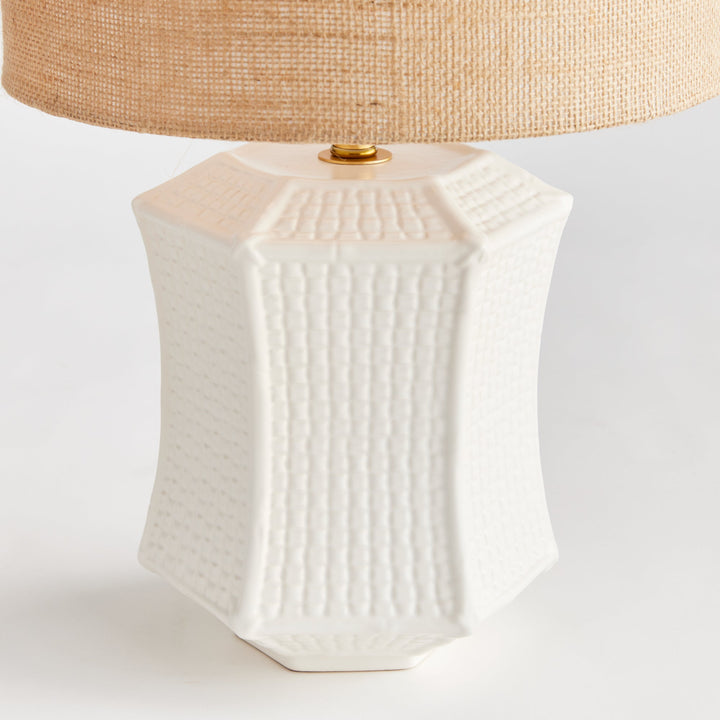 The ceramic base of this table lamp has a unique texture that resembles woven fabric, making it a defining feature of the piece. Its paneled design and impressive size make it a stand-out focal point for any transitional setting. Available in white and tan, this lamp adds an elegant touch to any room.