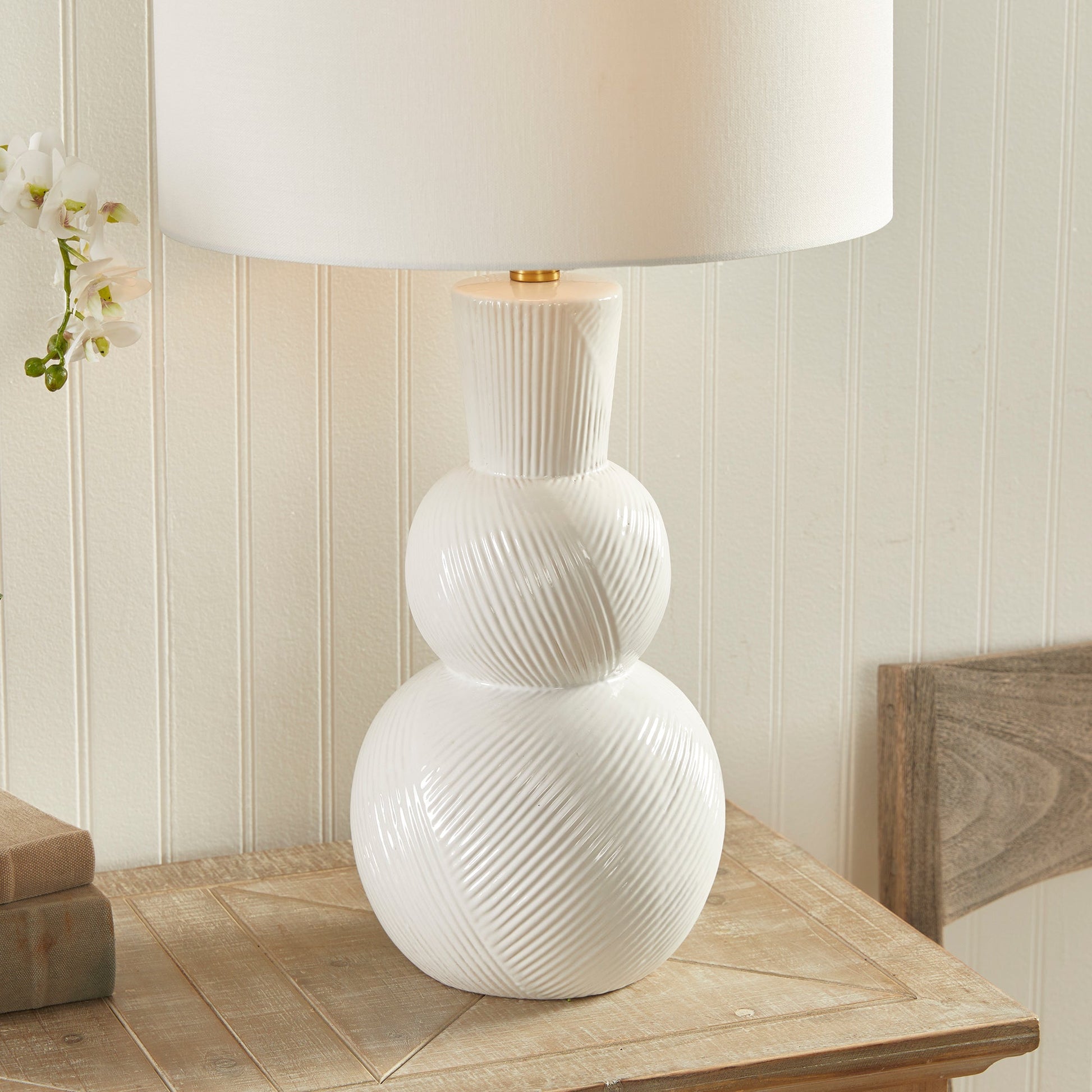 This traditional table lamp is crafted from clean white ceramic and features hand carved markings on the body, making it a perfect addition to any traditional setting. It is complemented by a white linen shade and a simple brass finial. Ideal for enhancing the ambiance of any living room or home decor.