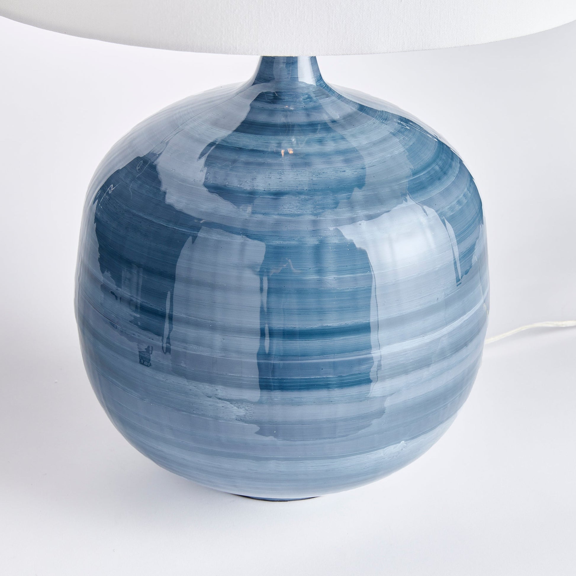 This blue table lamp features a unique design made of enameled iron and hand-painted for a lightweight yet elegant look. The horizontal swirl design adds a touch of refinement, while the oversized linen shade completes the modern aesthetic. A perfect addition to any contemporary living or dining space.