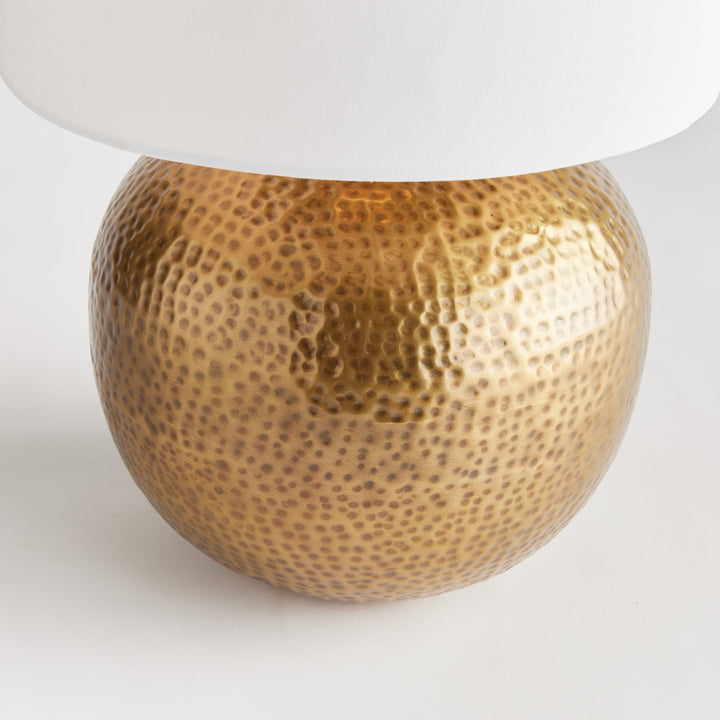 Enhance any room with the elegant style of Tara Gold &amp; White Table Lamp Small. The warm brass round base exudes a luxurious feel, while the crisp white linen drum shade offers a gentle radiance. Crafted from hammered iron and featuring unique handmade elements, this lamp is the perfect addition to any modern space.