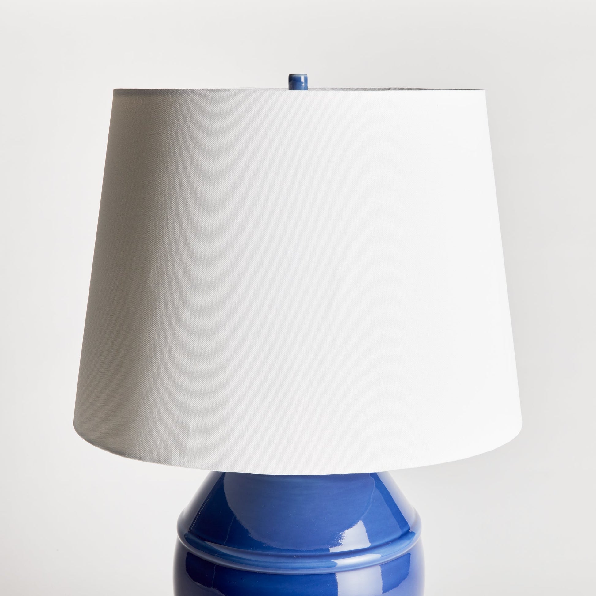 Constructed with a ceramic body and adorned with a deep, luxurious glaze, this coastal-inspired lamp exudes elegance. Enhancing its design, the wide drum shade is crafted from soft white linen, providing a striking contrast. Whether placed on a bedside table, console, or study desk, this lamp is a stunning and practical addition to any space. Its timeless blue and white color combination adds a touch of classic beauty.