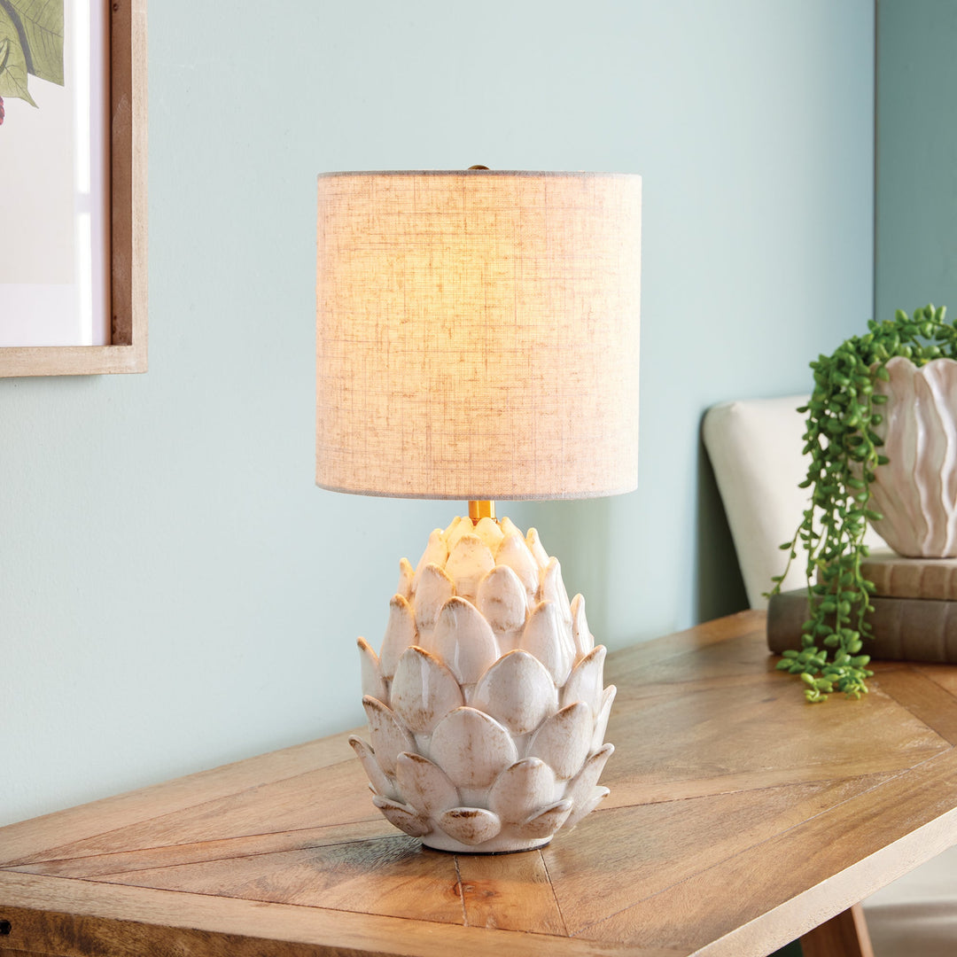 As an expert in this industry, I have designed a ceramic table lamp inspired by the natural beauty of an artichoke. Carefully hand-finished with antiqued edges, this masterpiece adds an elegant touch to traditional spaces. Paired with a natural linen shade, it is the perfect choice to elevate any room.