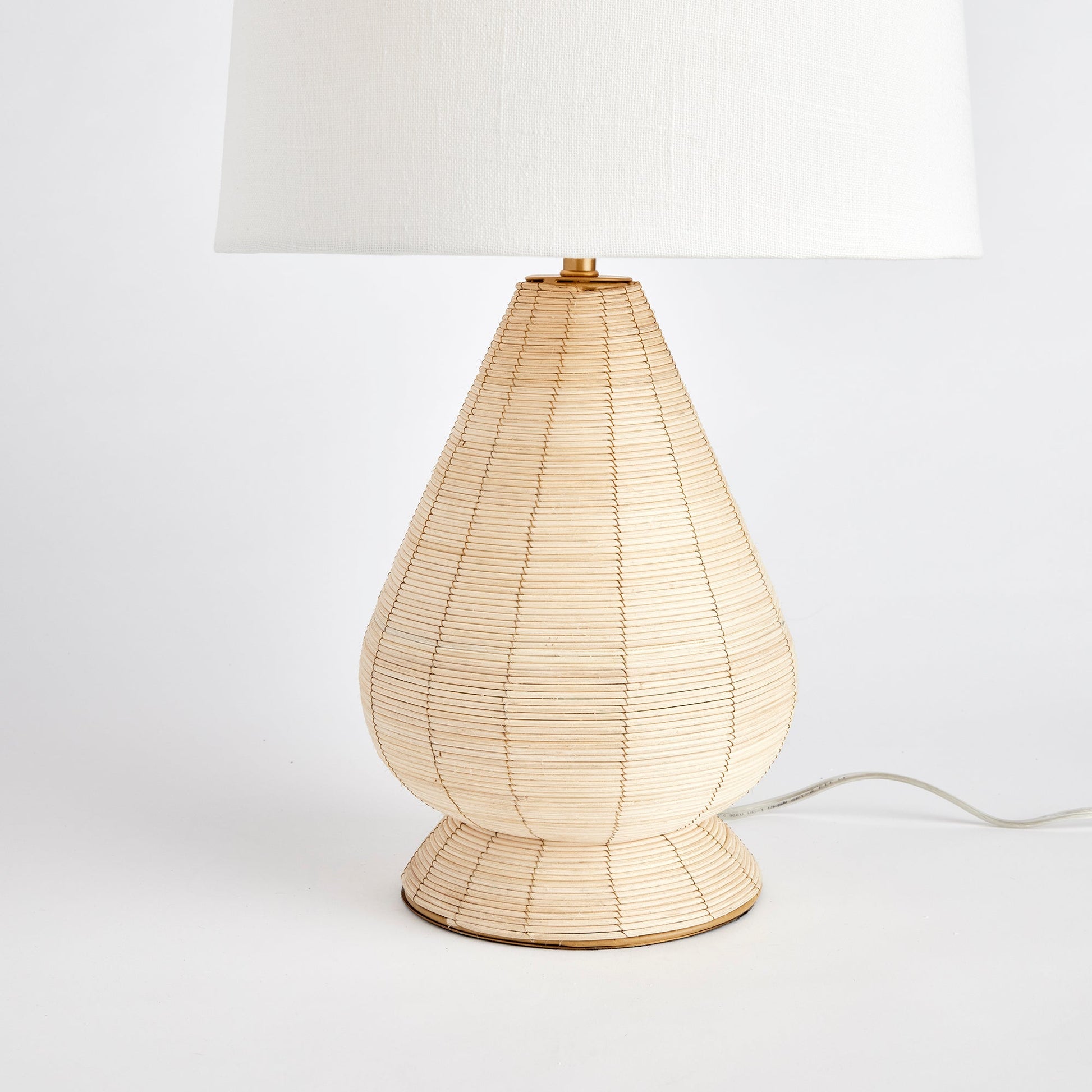 This table lamp features a whitewash cane rattan weave and each piece has its own unique color variations. It is a timeless piece complemented by a wide cylindrical shade, perfect for any bedroom, living room, or study. The lamp is handcrafted and features a European-style shade, making it a one-of-a-kind addition to any space.